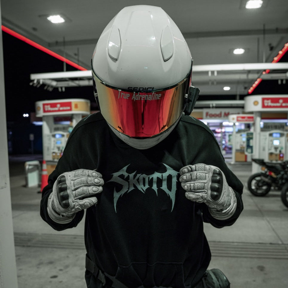 Helmeted rider with red visor presents the white chest graphic on a black hoodie at night.