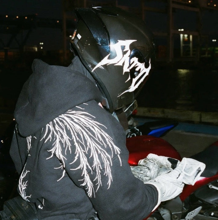 Helmeted rider wearing the black AUXESIS hoodie with white wing artwork across the back.