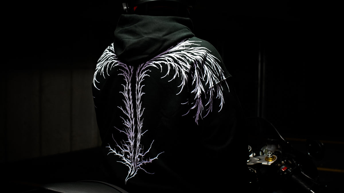 Close view of white branch-like artwork across the back of a black hoodie beside a motorcycle.